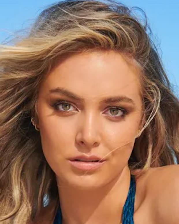 Raine Michaels poses in a blue halter neck swimsuit in front of the bright blue sky.
